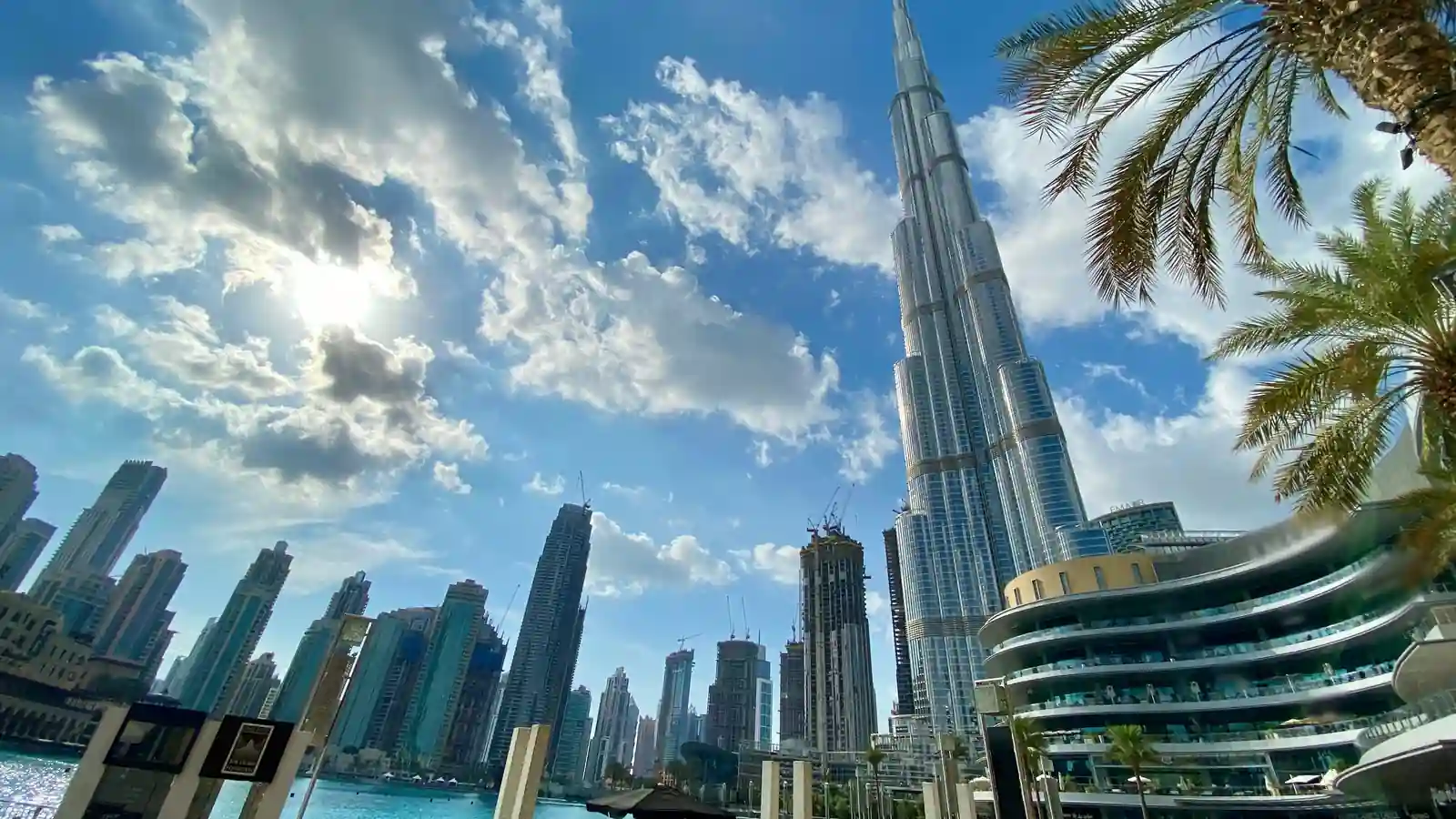 Low-angle daytime view of Burj Khalifa rising above Downtown Dubai with palm fronds in the foreground
