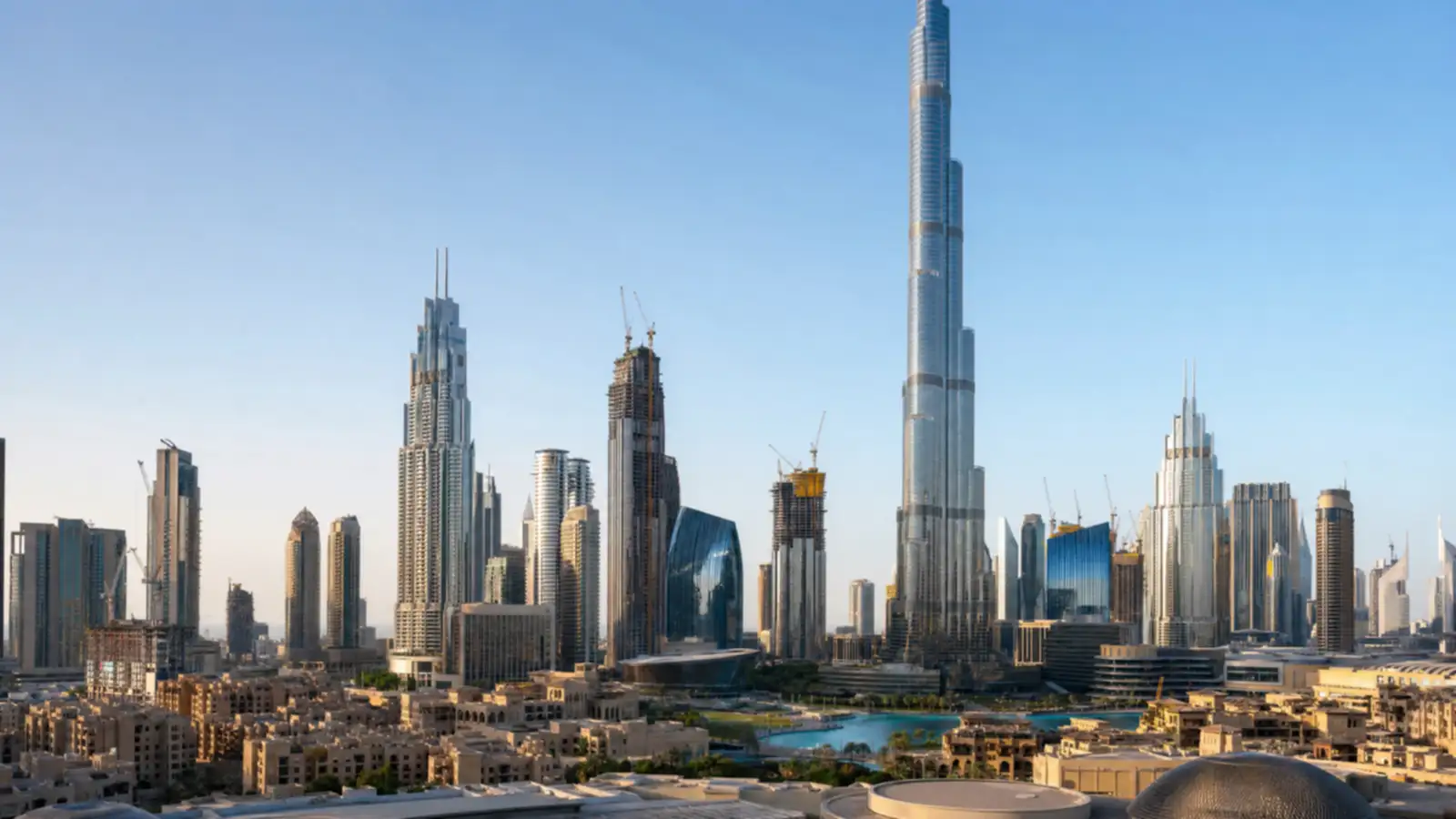 Downtown Dubai daytime skyline with Burj Khalifa and completed towers beside a high-rise building under construction with a crane