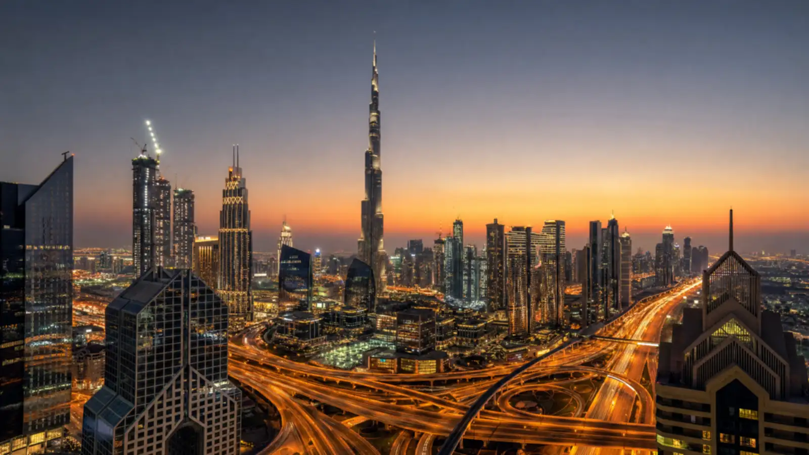 Wide elevated panorama of Dubai's dusk skyline with a dense cluster of illuminated towers