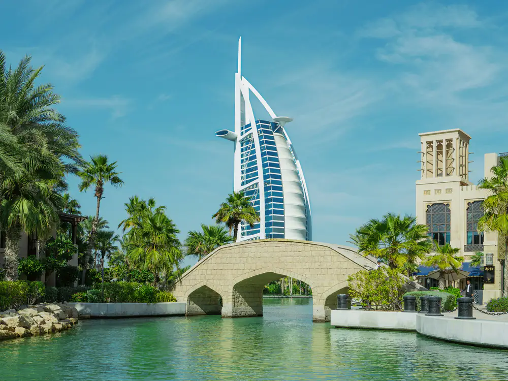 Burj Al Arab seen across the Madinat Jumeirah waterway, a stone bridge and palms in front